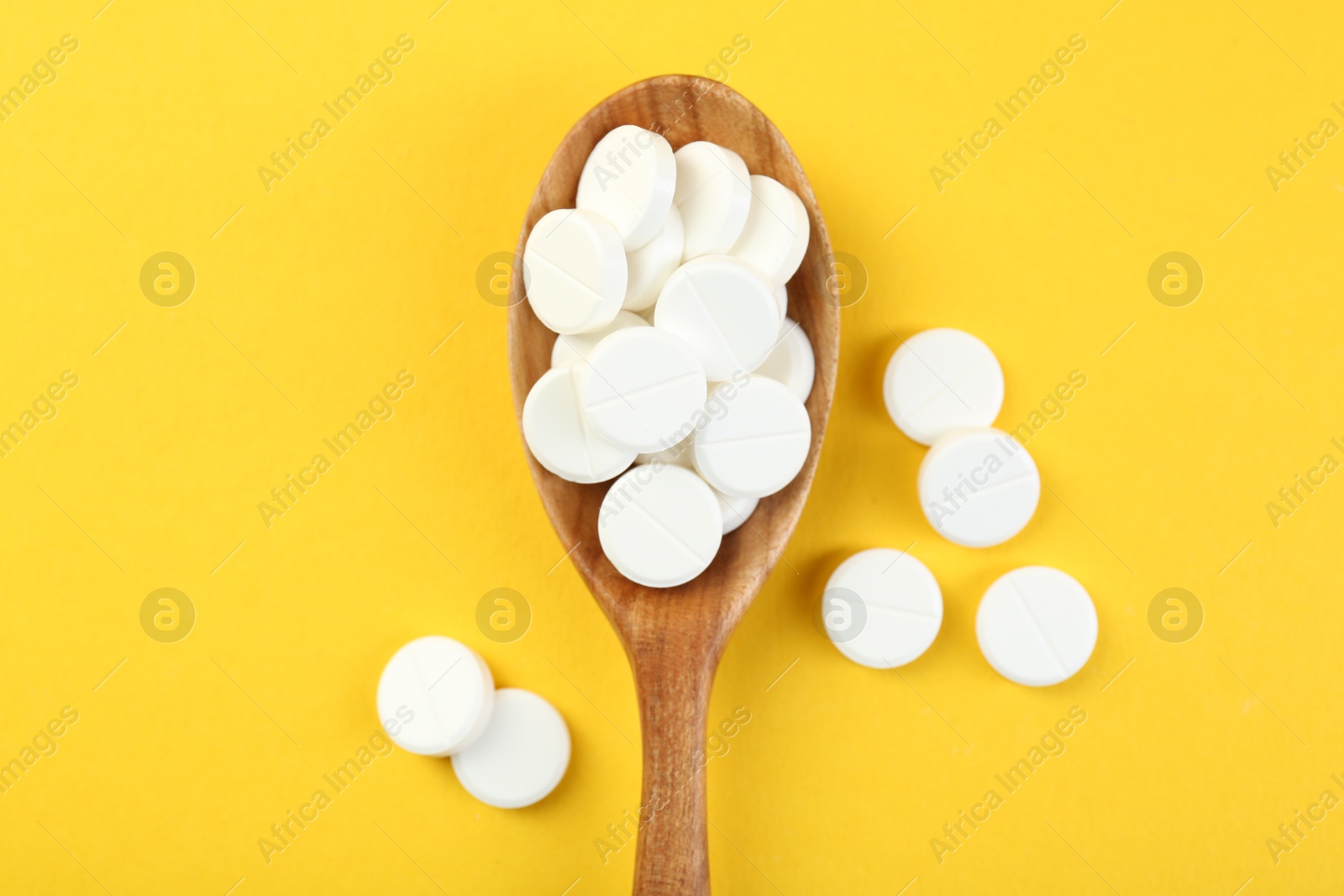 Photo of Antibiotic pills in spoon on yellow background, top view