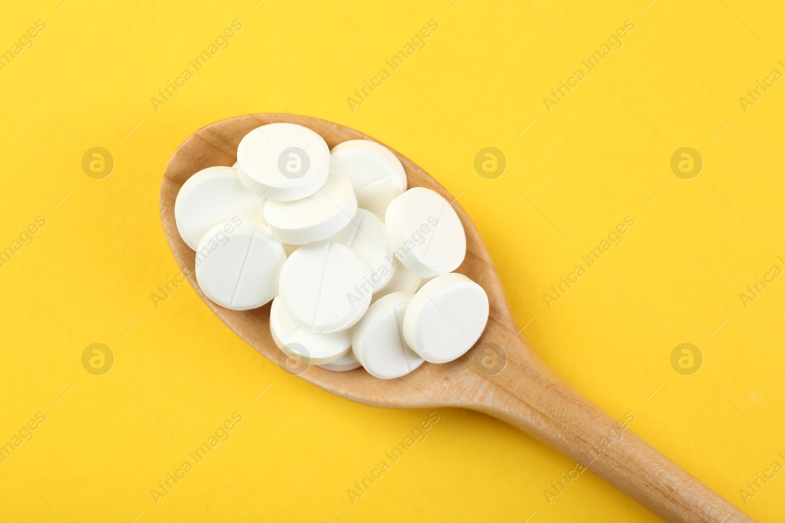 Photo of Antibiotic pills in spoon on yellow background, top view