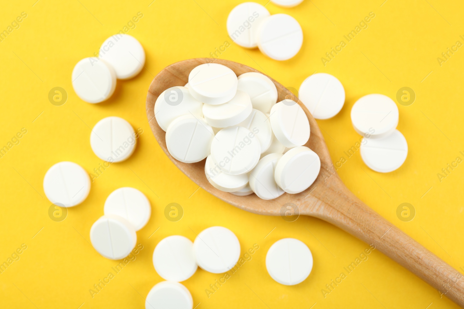 Photo of Antibiotic pills in spoon on yellow background, top view