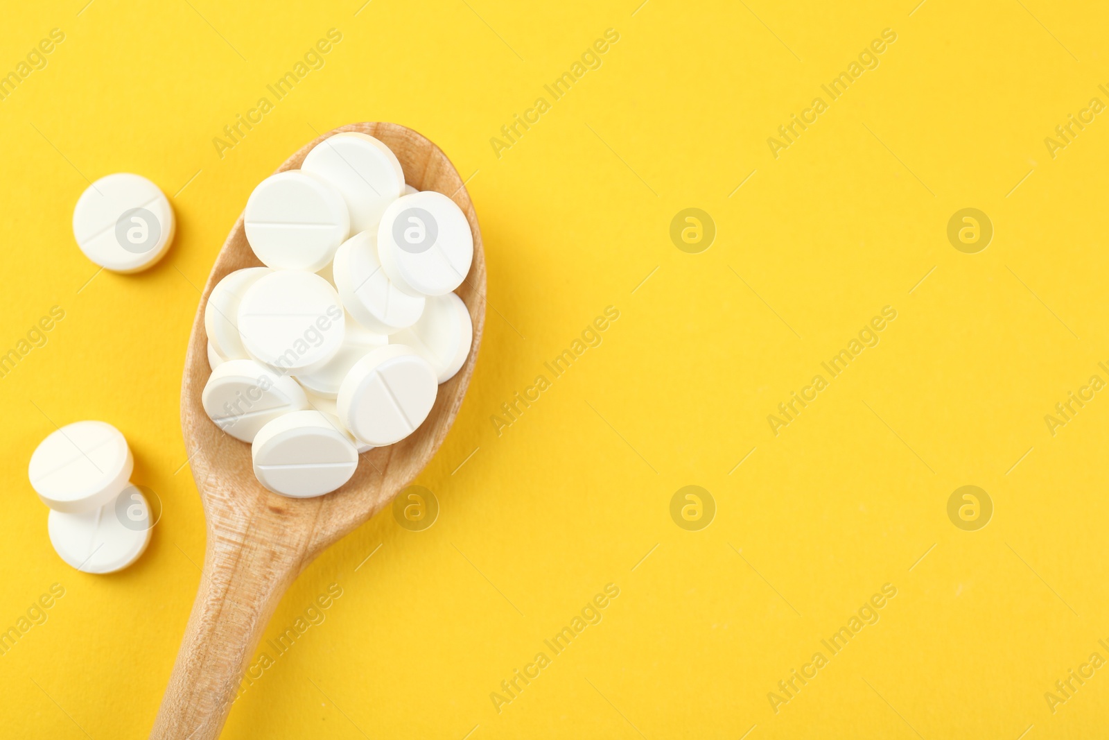 Photo of Antibiotic pills in spoon on yellow background, top view. Space for text