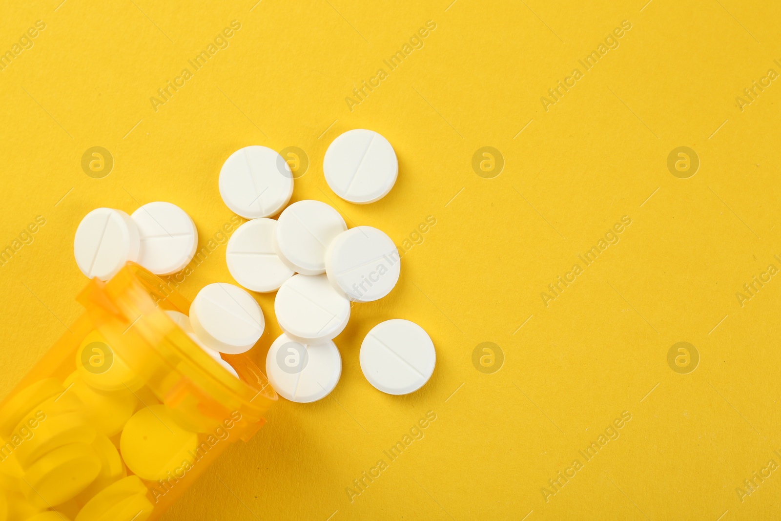 Photo of Medical bottle with antibiotic pills on yellow background, top view