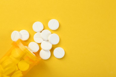 Photo of Medical bottle with antibiotic pills on yellow background, top view