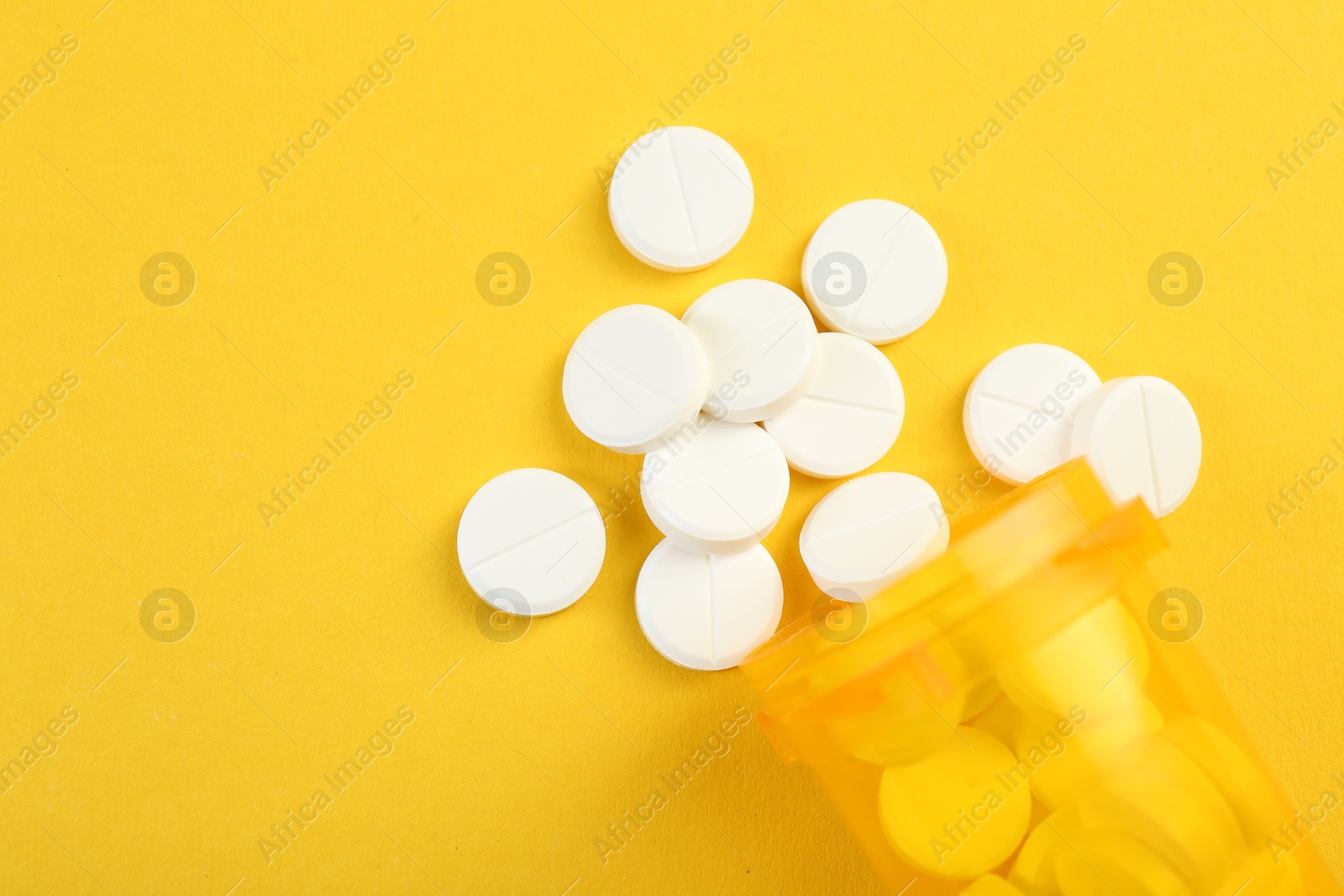 Photo of Medical bottle with antibiotic pills on yellow background, top view