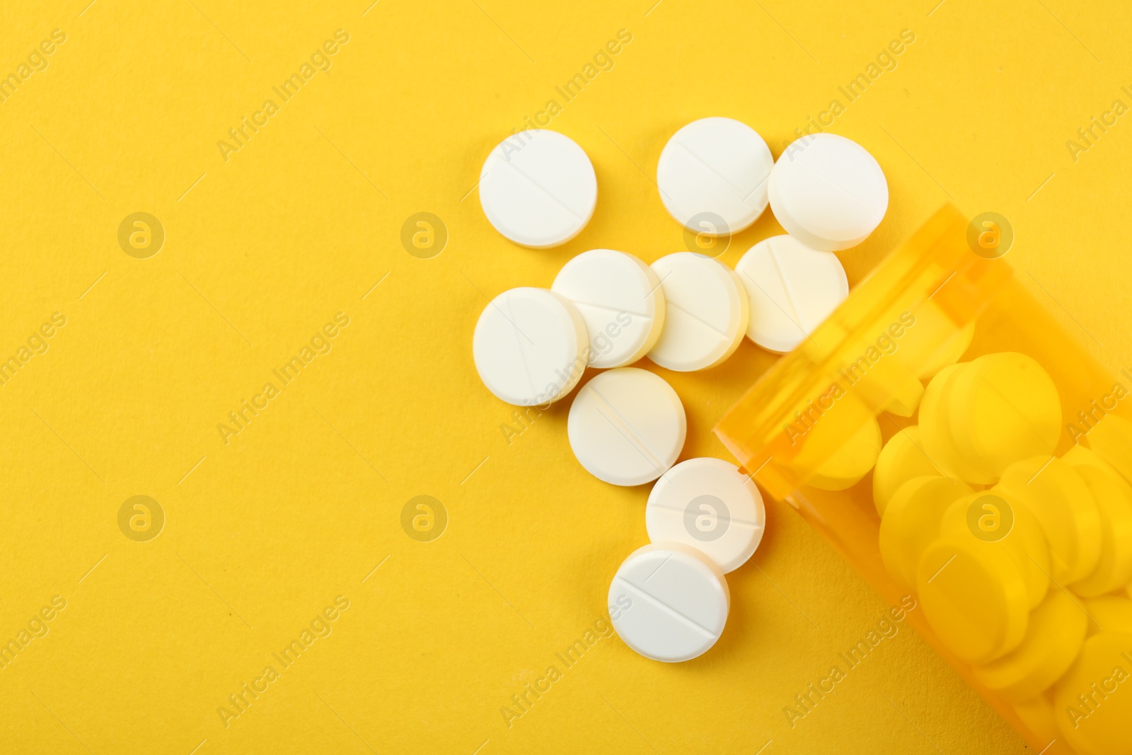 Photo of Medical bottle with antibiotic pills on yellow background, top view. Space for text