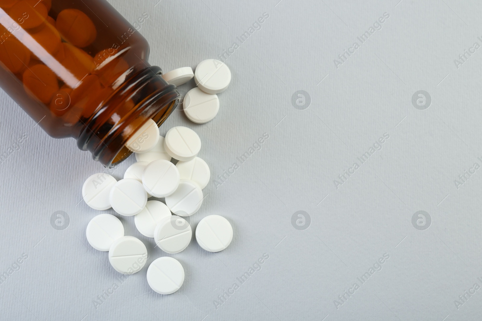 Photo of Medical bottle with antibiotic pills on grey background, top view. Space for text