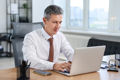 Photo of Middle aged man working with laptop at table in office