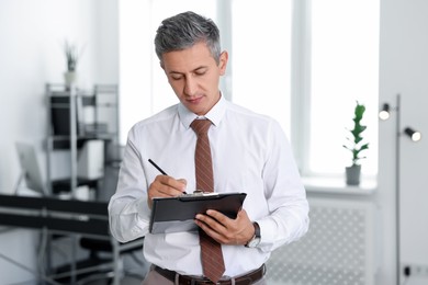 Photo of Middle aged man working with clipboard in office