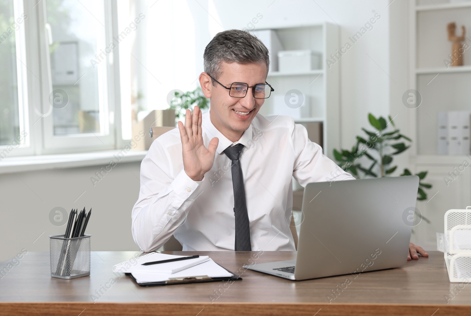 Photo of Smiling middle aged man having videochat via laptop at table in office