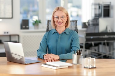 Photo of Portrait of smiling middle aged woman at table in office