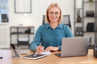 Photo of Smiling middle aged woman working with laptop at table in office