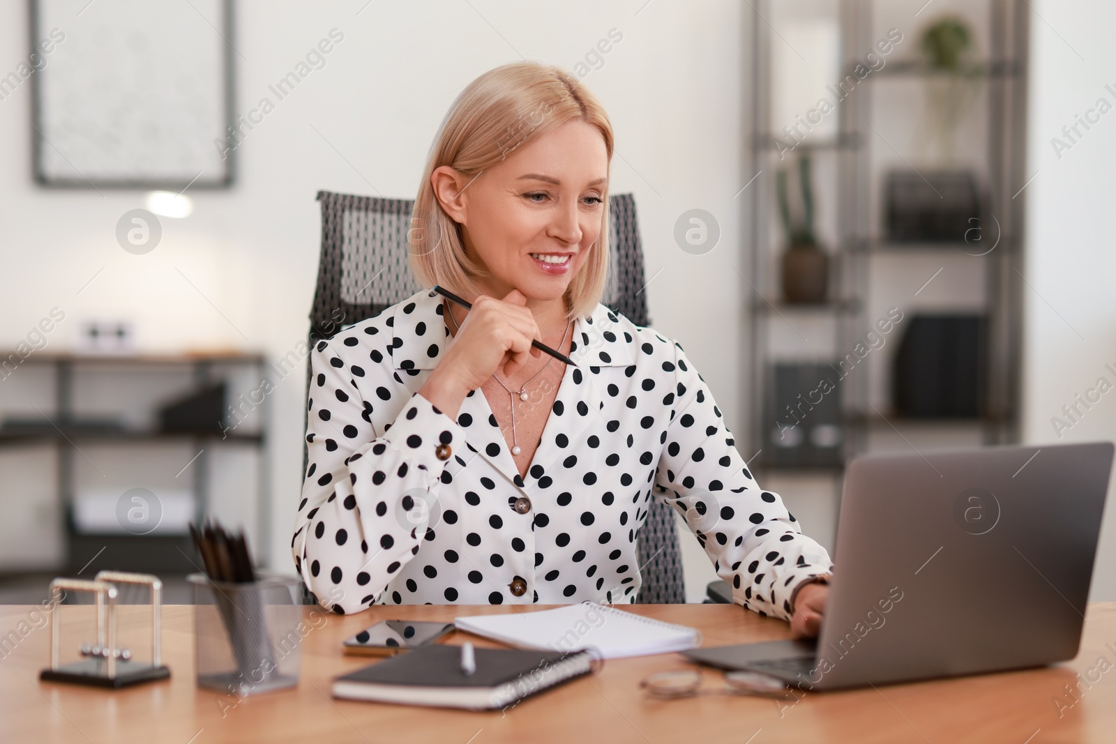 Photo of Smiling middle aged woman working with laptop at table in office