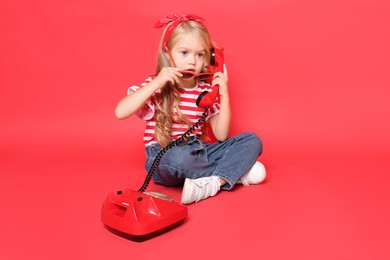 Cute little girl with telephone on red background