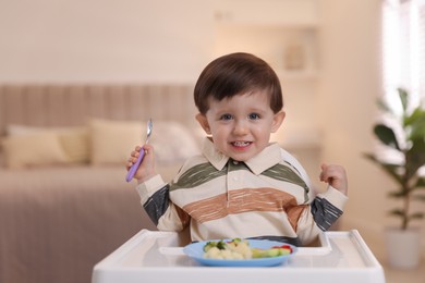 Cute little baby eating healthy food in high chair at home