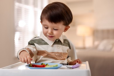 Photo of Cute little baby eating healthy food in high chair at home