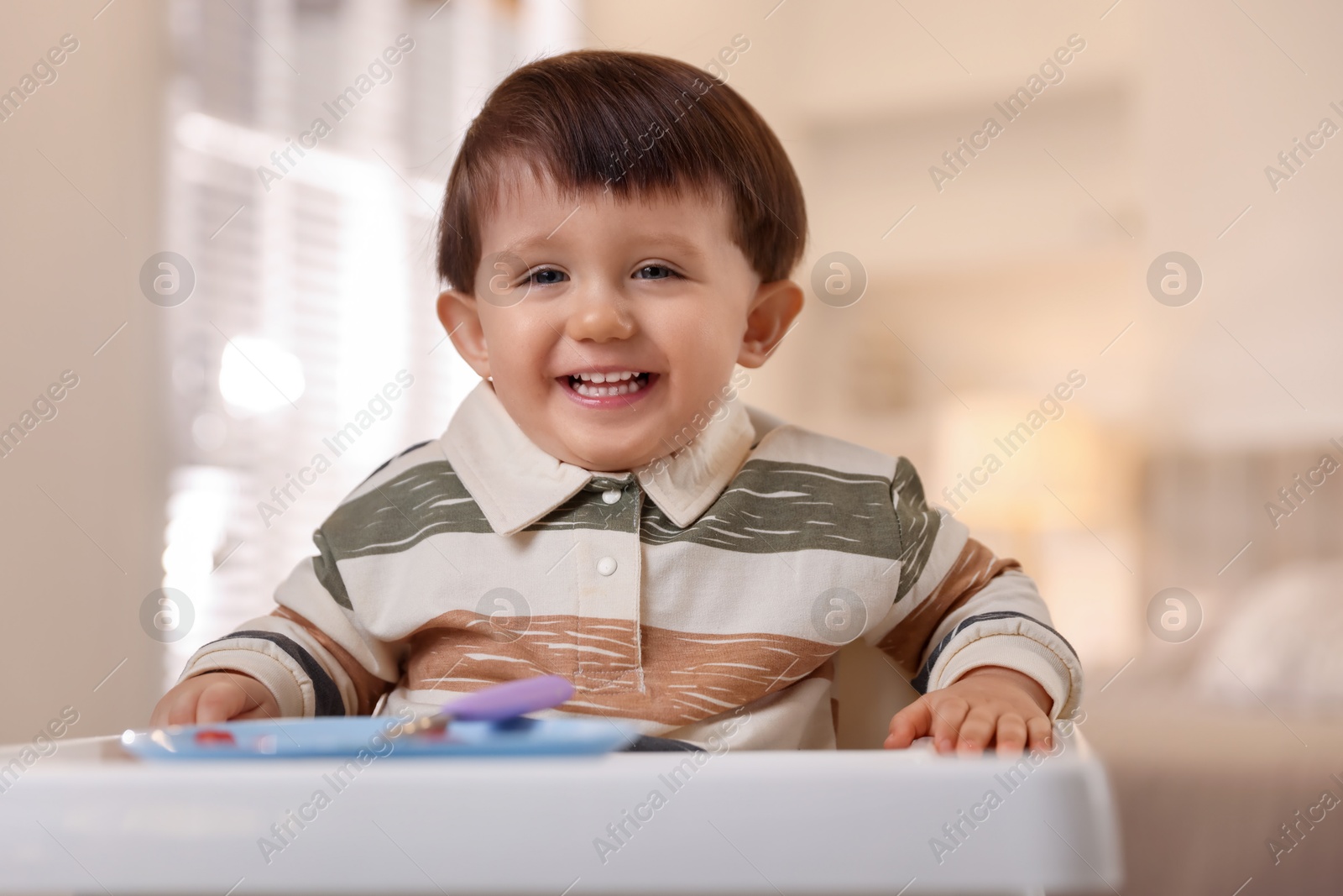 Photo of Cute little baby eating healthy food in high chair at home