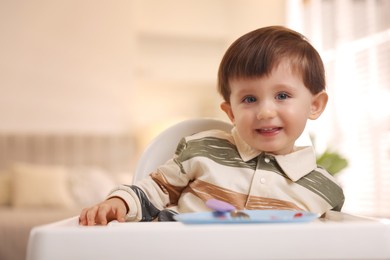 Cute little baby eating healthy food in high chair at home