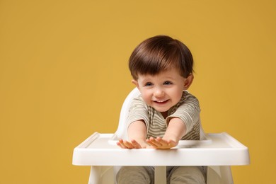 Photo of Cute little kid sitting in high chair on yellow background