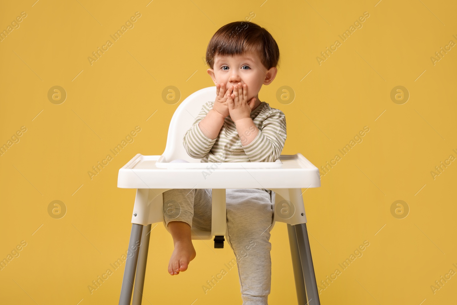 Photo of Cute little kid sitting in high chair on yellow background