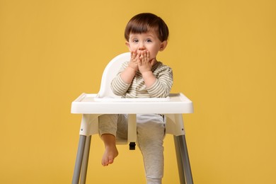 Photo of Cute little kid sitting in high chair on yellow background