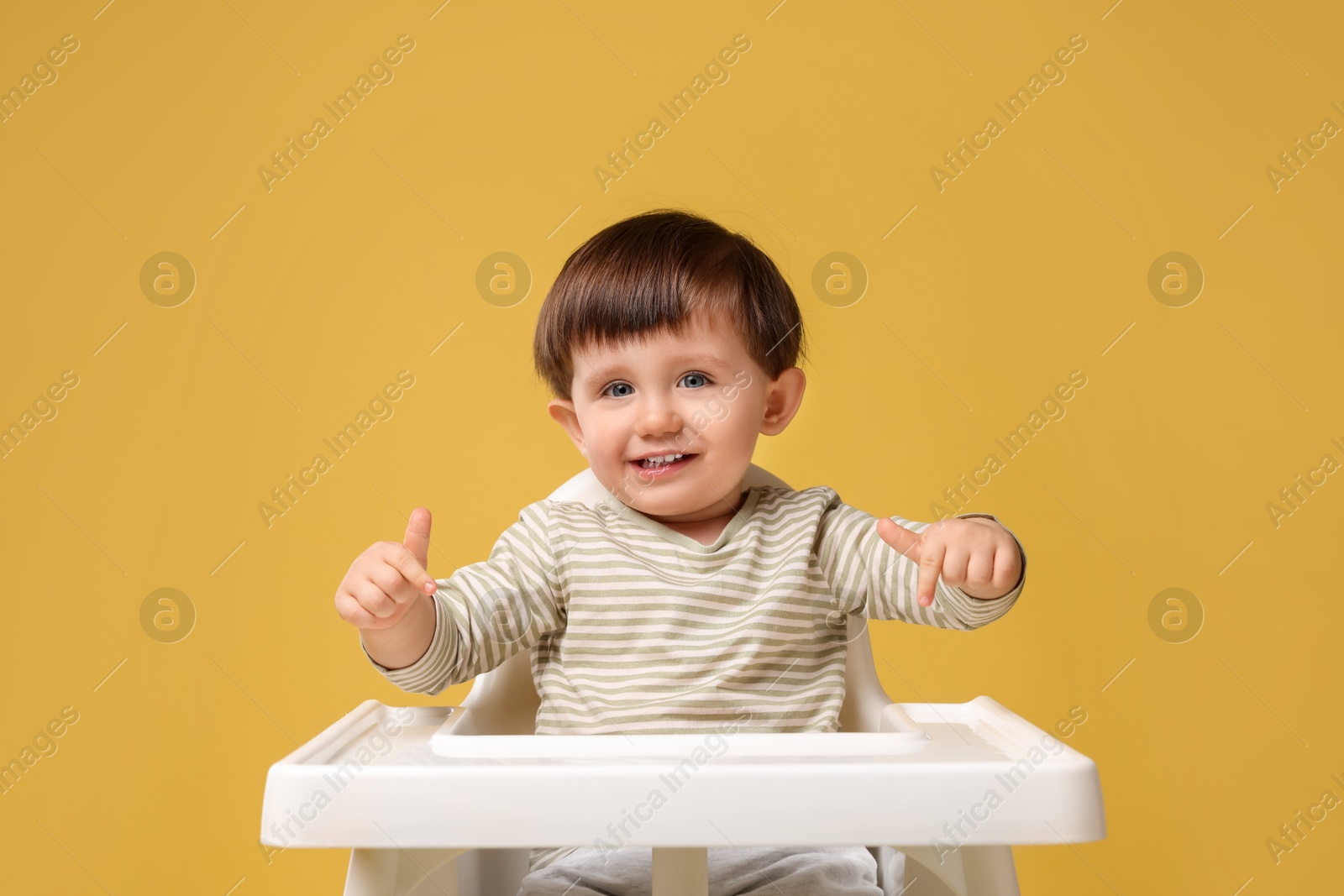 Photo of Cute little kid sitting in high chair on yellow background