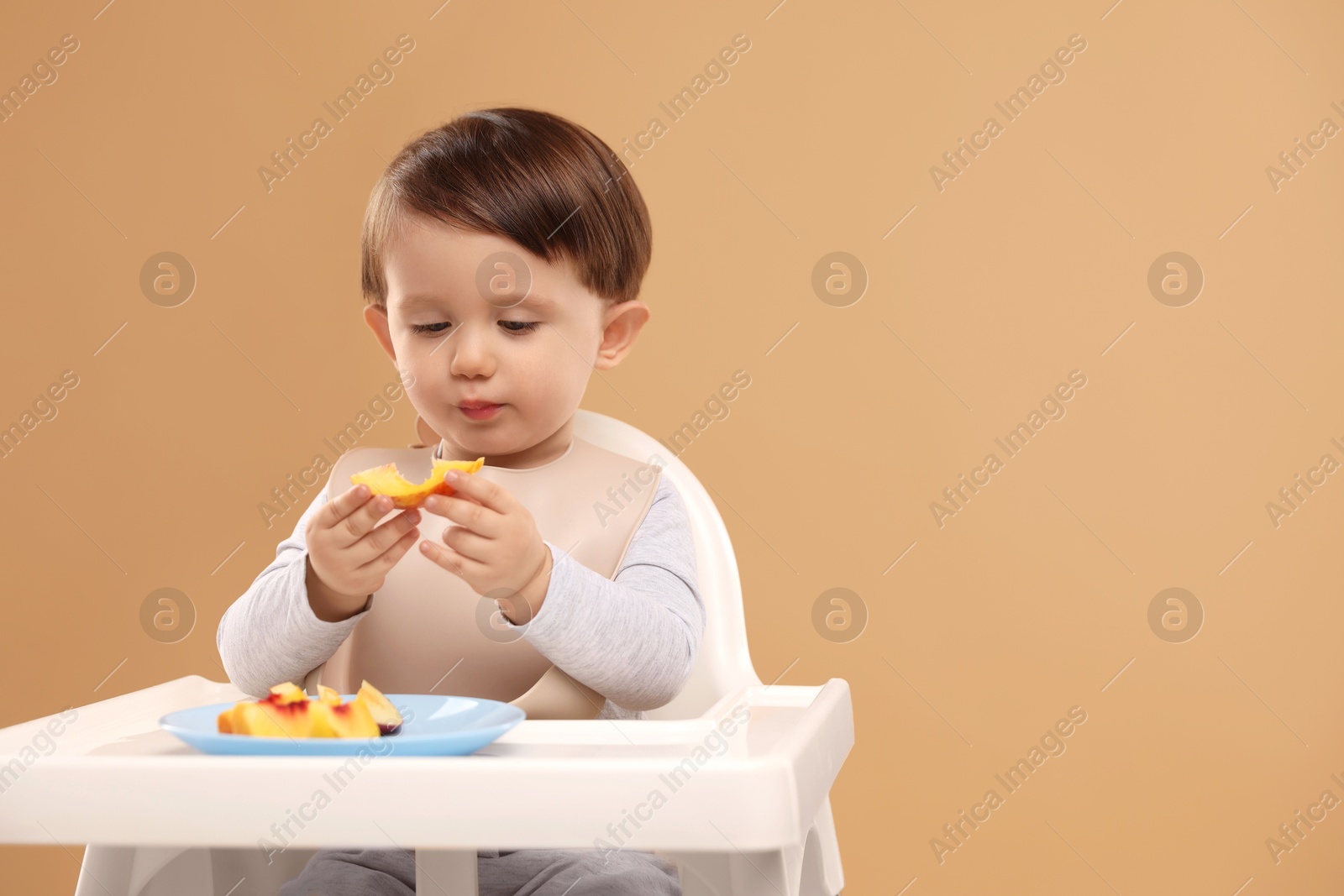 Photo of Healthy baby food. Cute little kid eating fruits in high chair on beige background, space for text