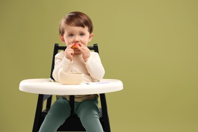 Photo of Cute little baby eating healthy food from bowl in high chair on olive background, space for text