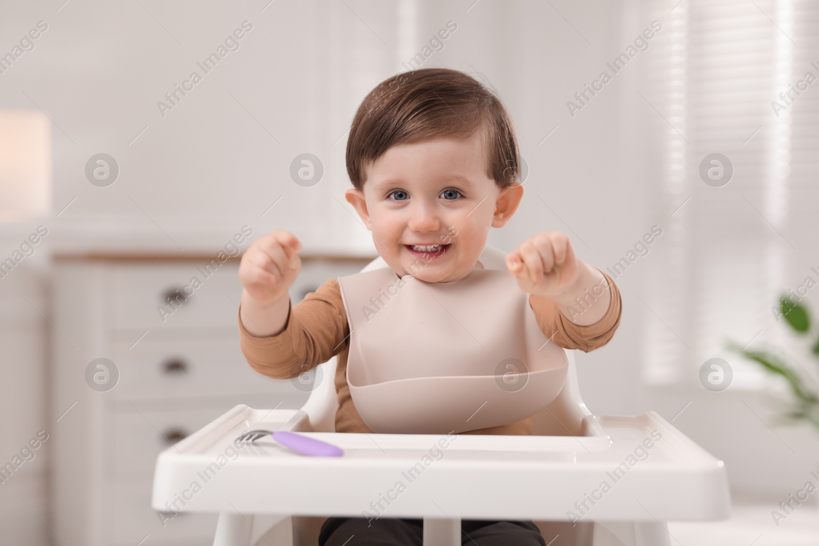 Photo of Cute little kid with fork sitting in high chair at home