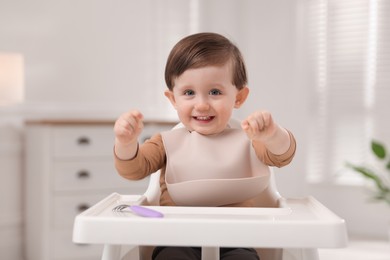 Cute little kid with fork sitting in high chair at home