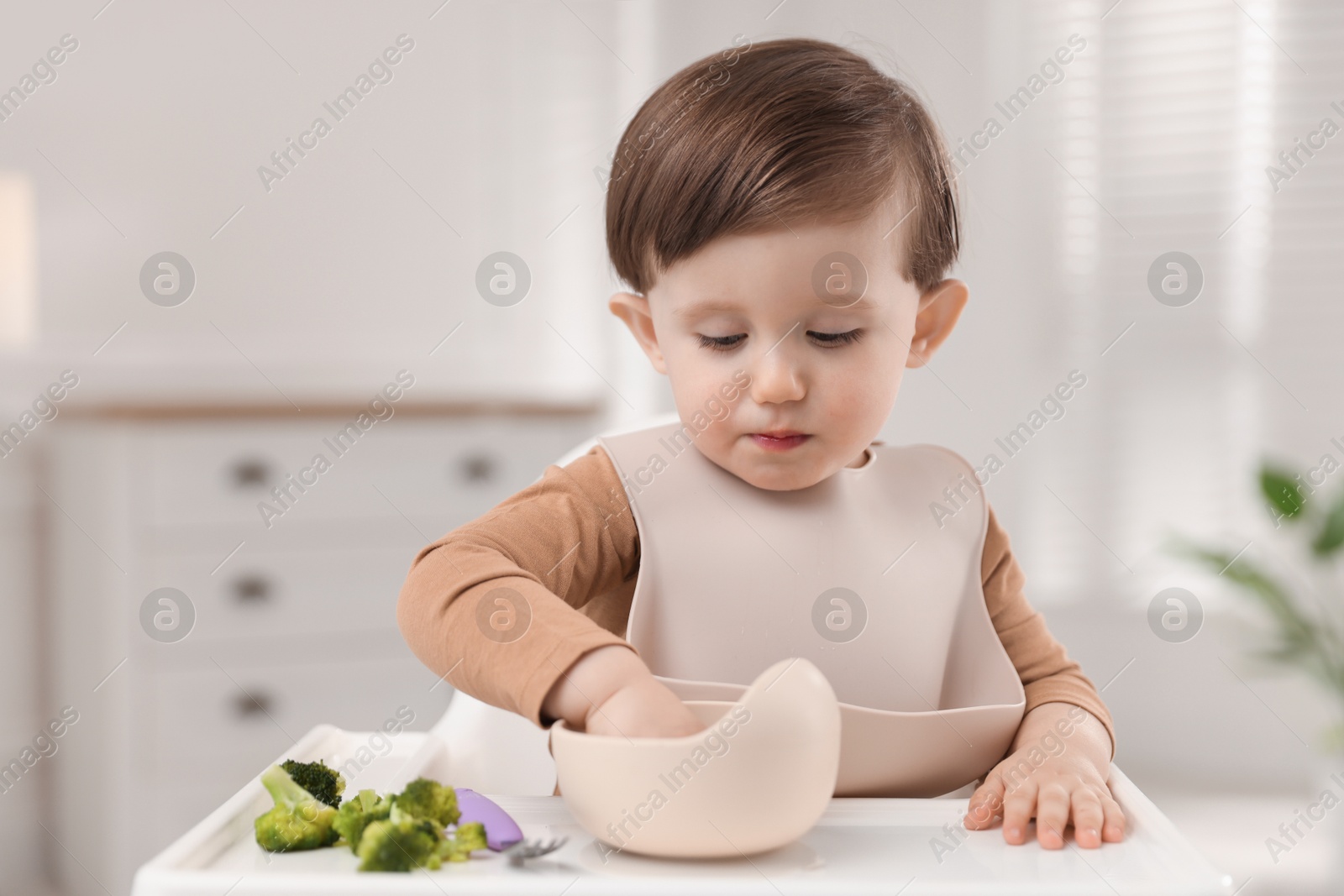 Photo of Cute little baby eating healthy food from bowl in high chair at home