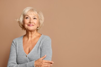 Portrait of beautiful senior woman on light brown background, space for text