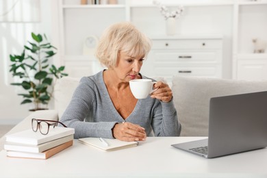 Photo of Beautiful senior woman using laptop at white table indoors