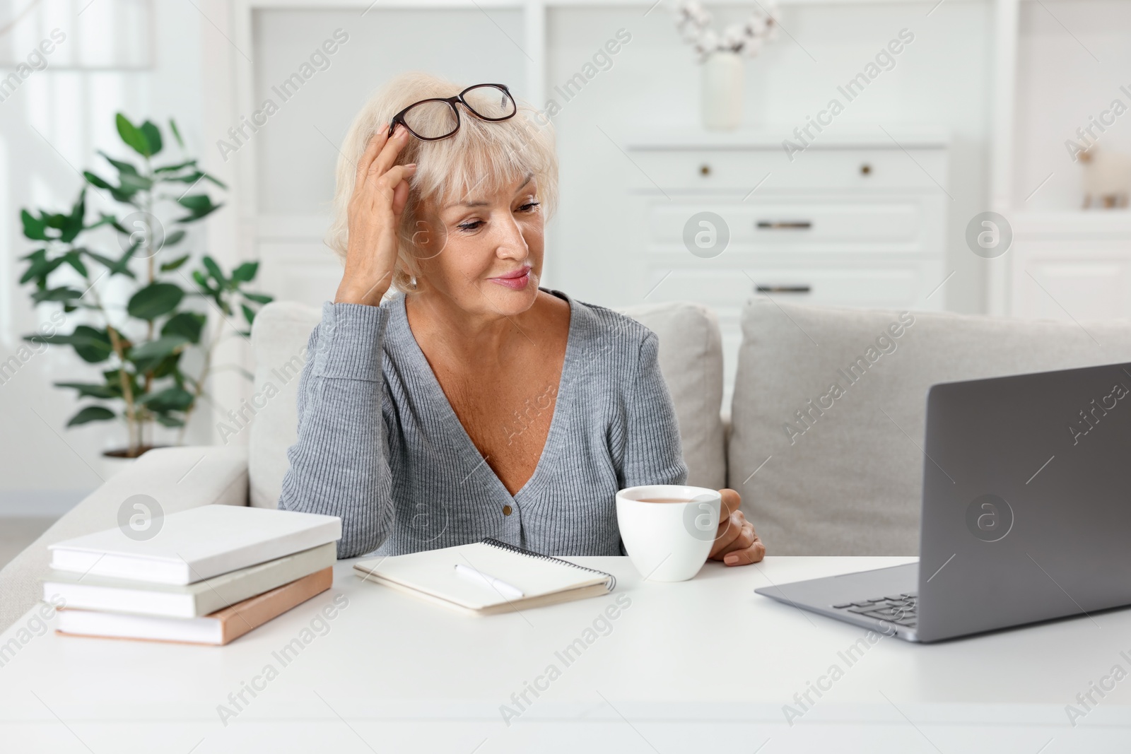 Photo of Beautiful senior woman using laptop at white table indoors