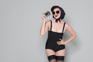 Photo of Pin-up woman in sunglasses with camera on grey background, space for text