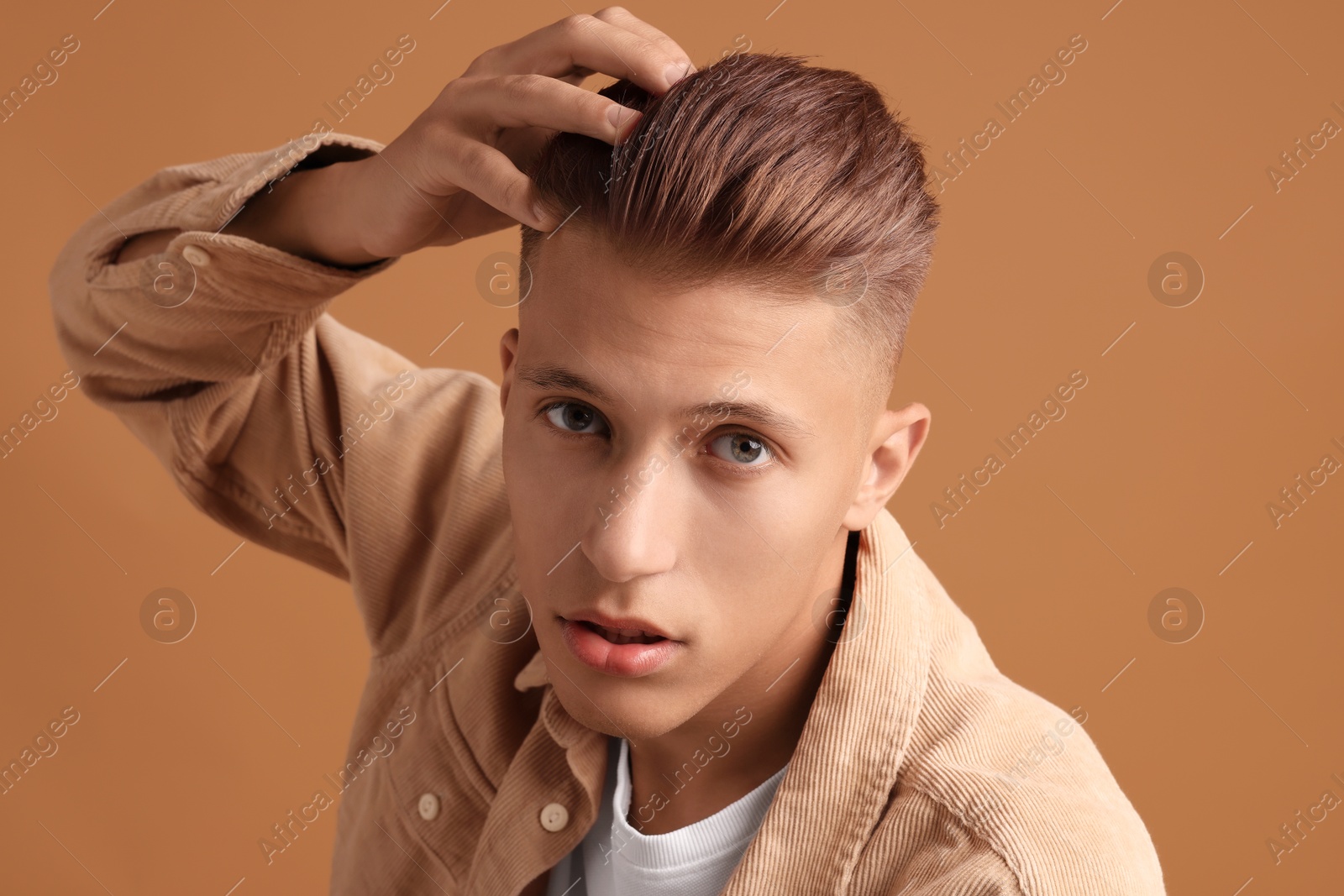 Photo of Confident young man with stylish haircut on brown background