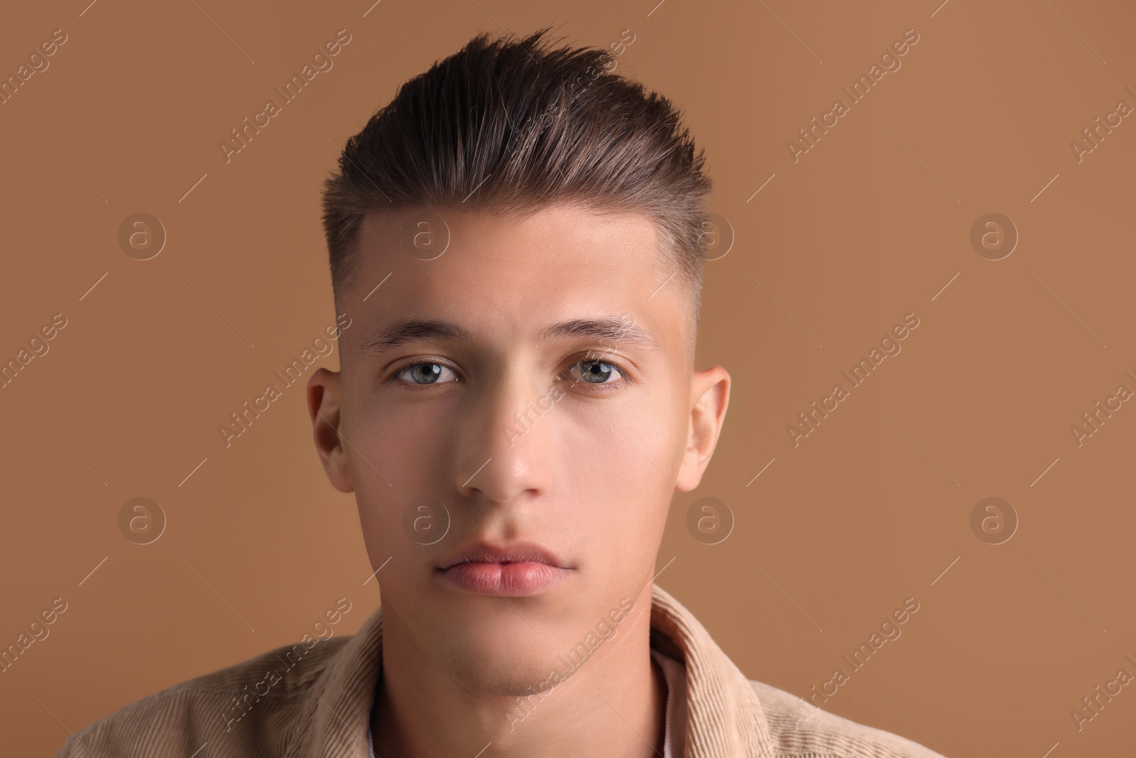 Photo of Confident young man with stylish haircut on brown background