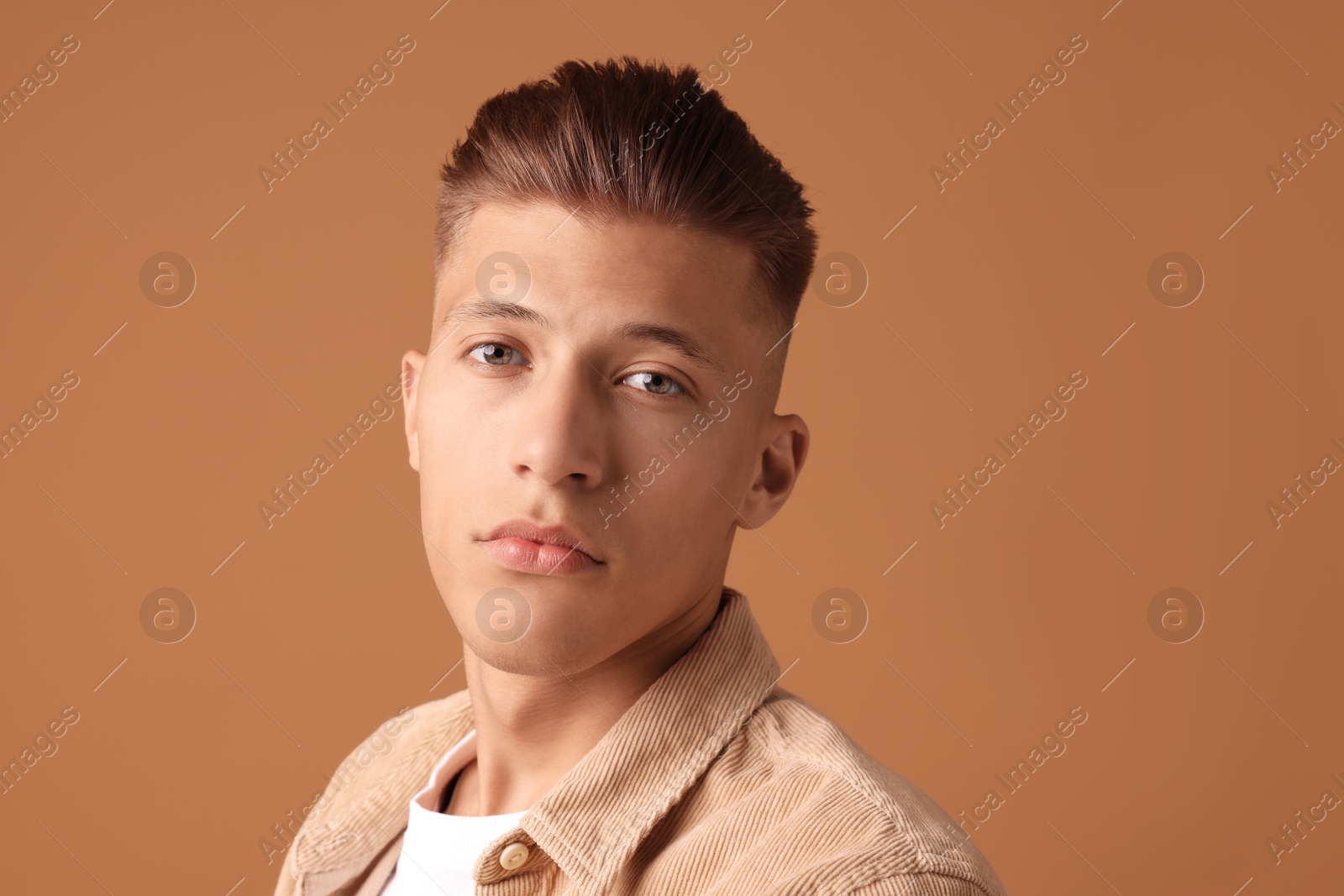 Photo of Confident young man with stylish haircut on brown background