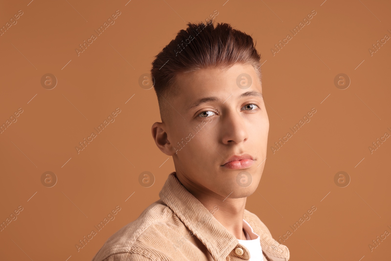 Photo of Confident young man with stylish haircut on brown background