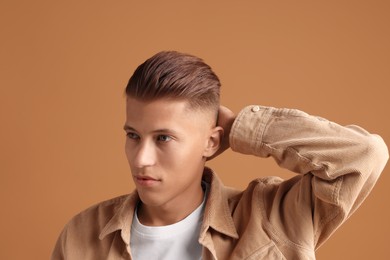 Photo of Confident young man with stylish haircut on brown background