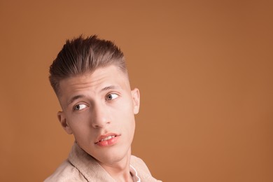 Photo of Confident young man with stylish haircut on brown background. Space for text