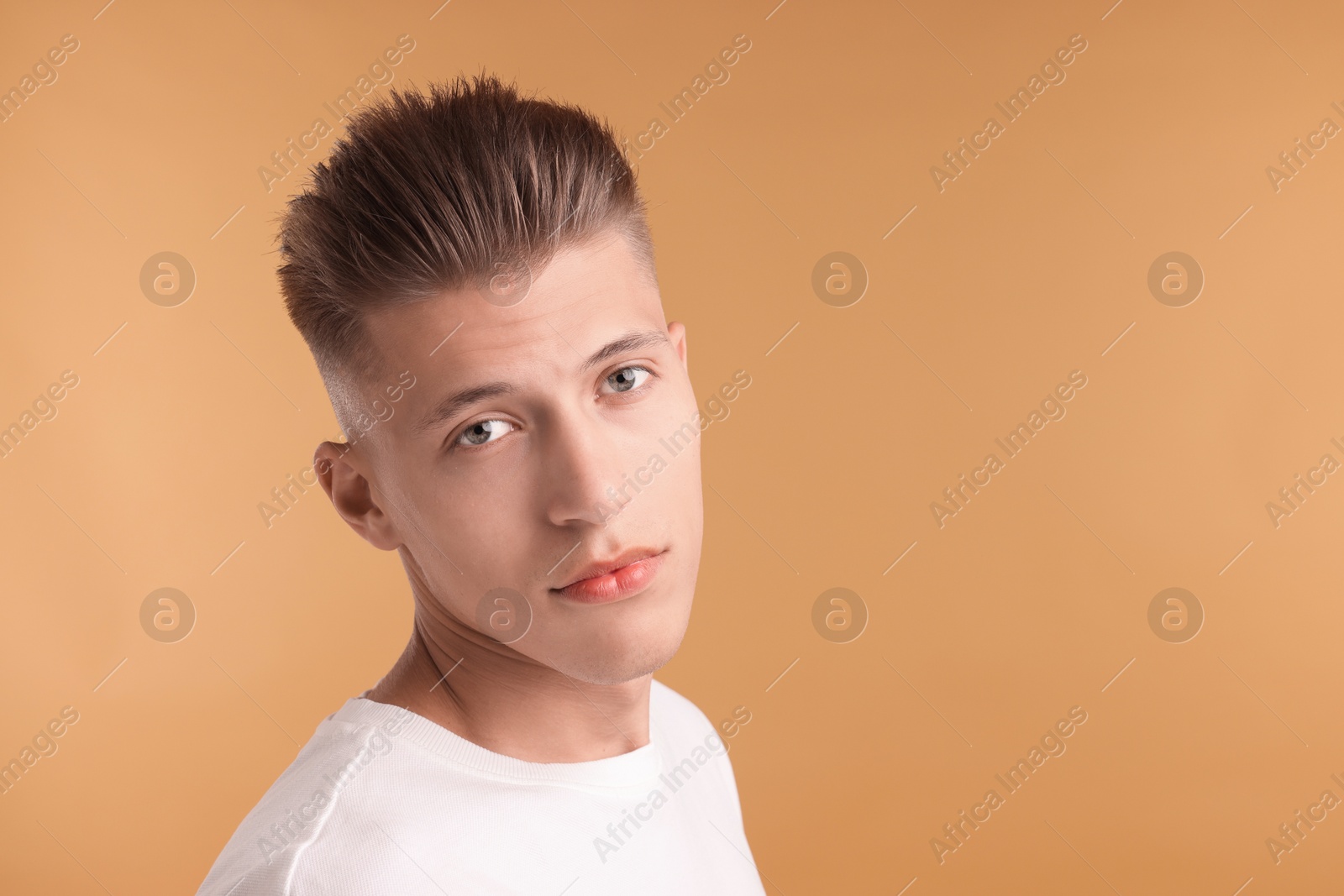 Photo of Confident young man with stylish haircut on light brown background. Space for text