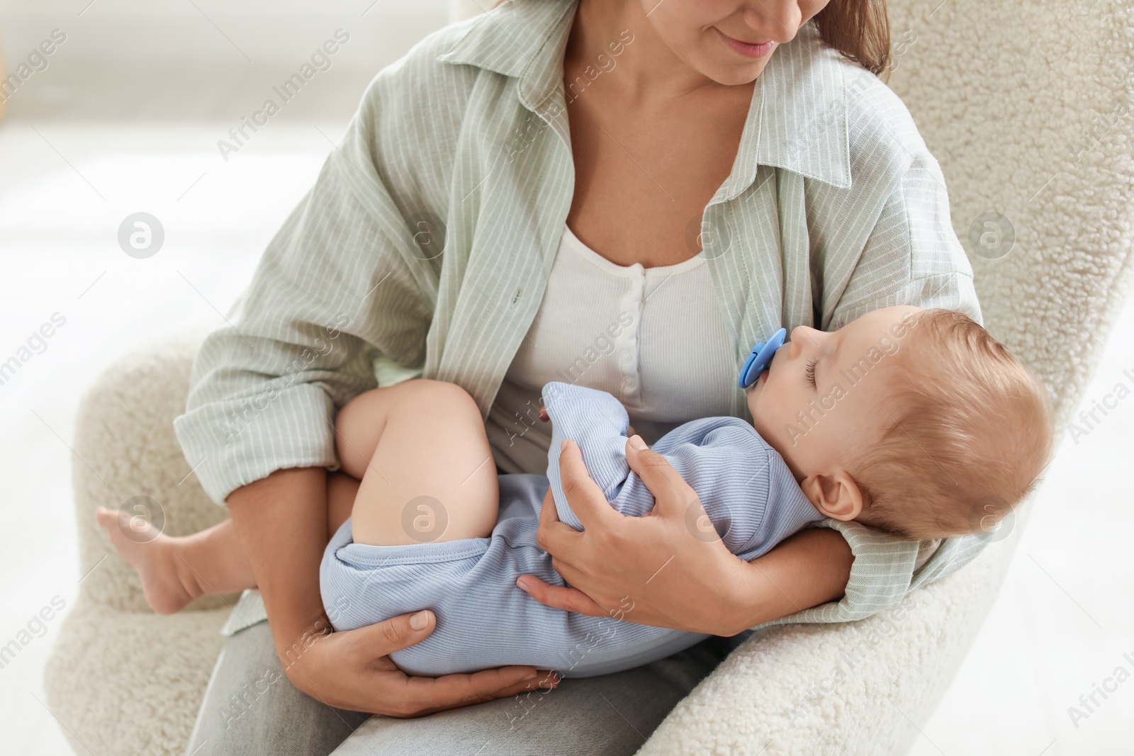 Photo of Mother with her sleeping baby in armchair indoors, closeup