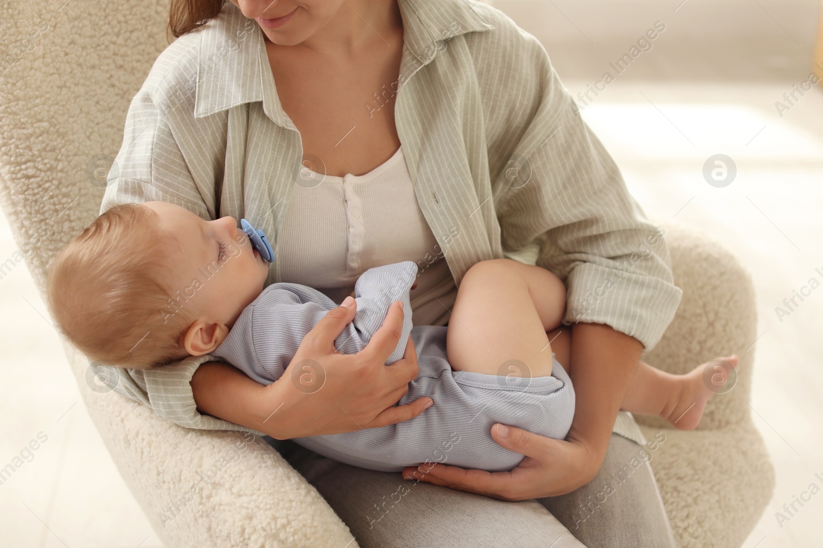 Photo of Mother with her sleeping baby in armchair indoors, closeup