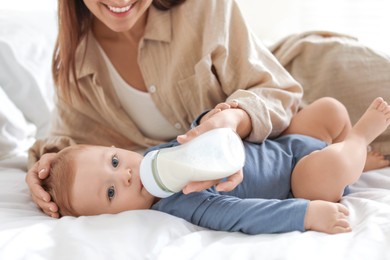 Mother feeding her little baby from bottle on bed indoors, closeup