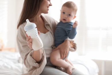 Photo of Mother holding cute little baby and bottle of milk on bed at home, selective focus