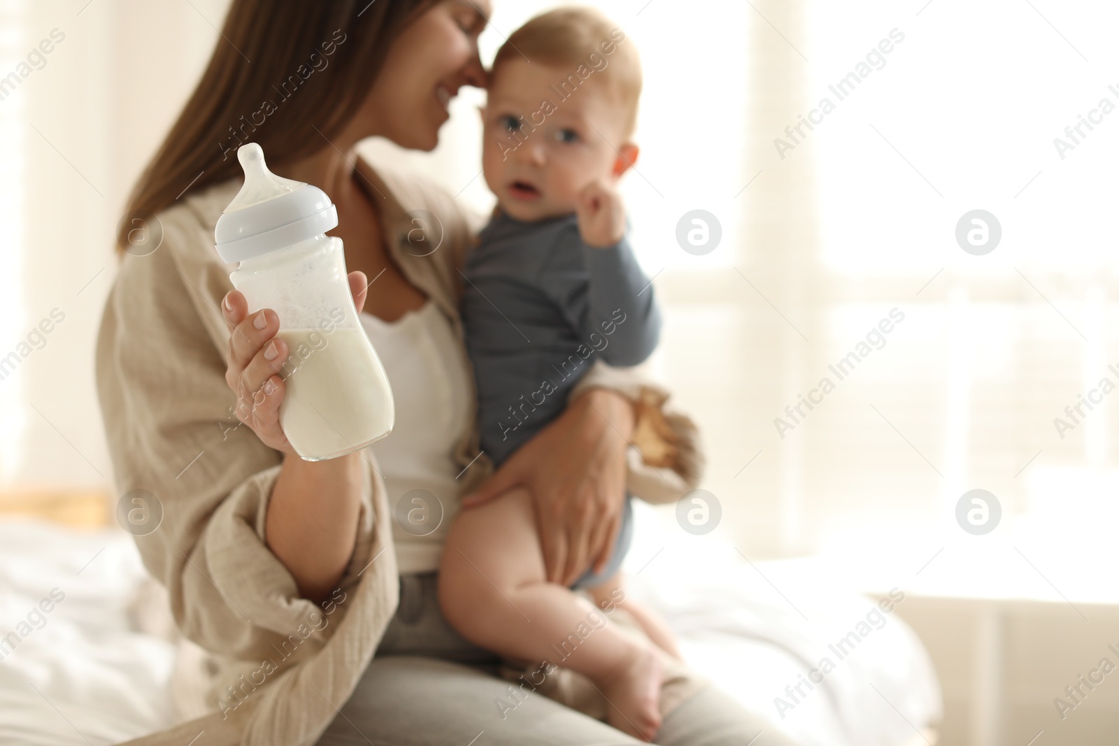 Photo of Mother holding cute little baby and bottle of milk on bed at home, selective focus. Space for text