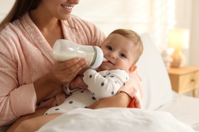 Photo of Mother feeding her little baby from bottle on bed at home, closeup