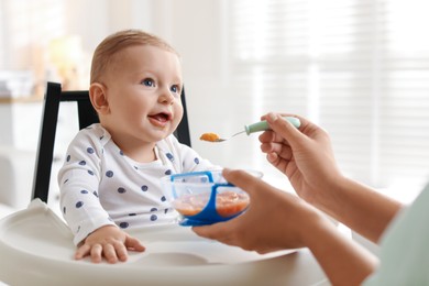 Photo of Mother feeding her cute little baby in high chair at home, closeup