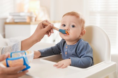 Photo of Mother feeding her cute little baby in high chair at home, closeup