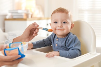 Photo of Mother feeding her cute little baby in high chair at home, closeup