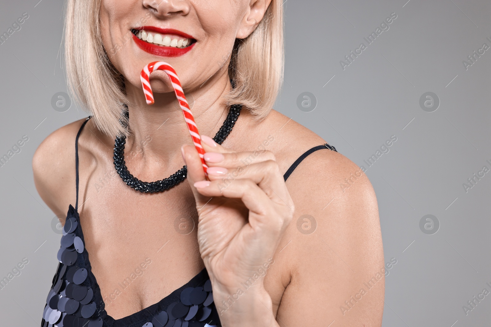 Photo of Smiling woman with Christmas candy cane on grey background, closeup